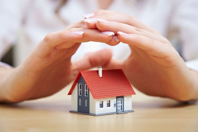 Manos protegiendo una casa en miniatura